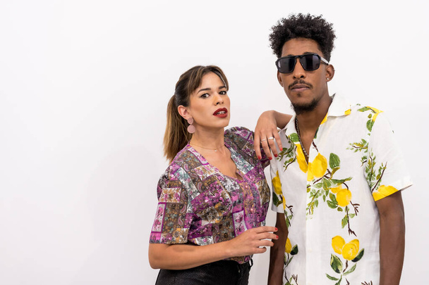 Couple of a black boy and a Caucasian girl on a white background, floral shirts, posed looking at the camera - Photo, Image