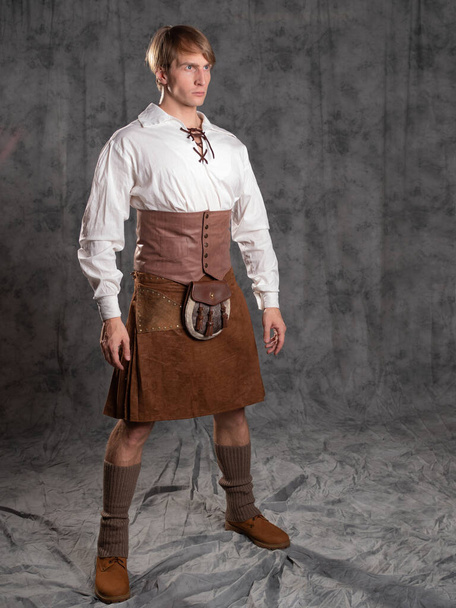 A young man in a leather kilt and a white lace-up blouse. A Scottish knight - Φωτογραφία, εικόνα