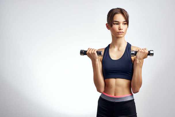 athletic woman with dumbbells in hand with workout exercises light background - Fotoğraf, Görsel
