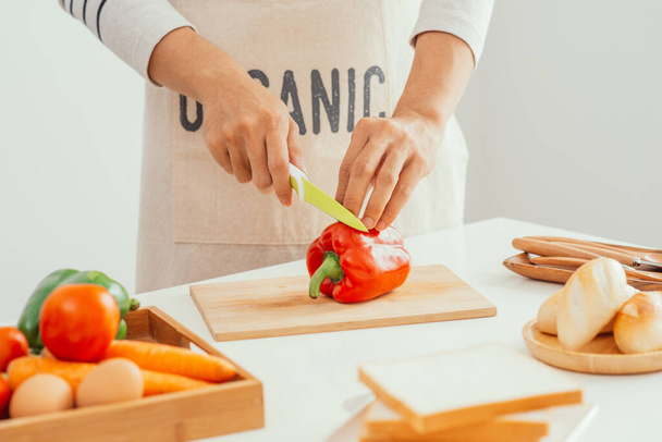 Man handen snijden verse pepers met scherp mes in de keuken - Foto, afbeelding