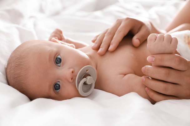 Mother and her cute little baby with pacifier on bed, closeup - Foto, immagini