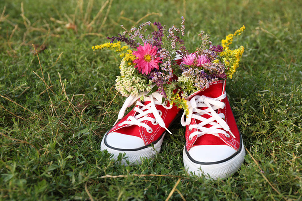 Shoes with beautiful flowers on grass outdoors - Zdjęcie, obraz