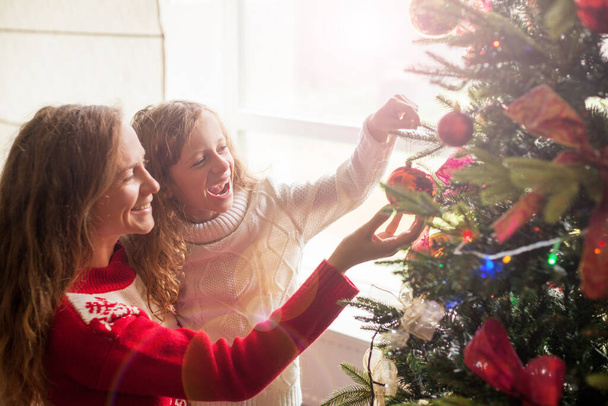 Mom and daughter decorate the Christmas tree. Happy family at home - Foto, imagen
