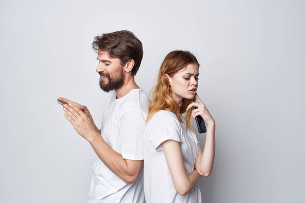 married couple in white T-shirts with phones in their hands light background - Fotoğraf, Görsel