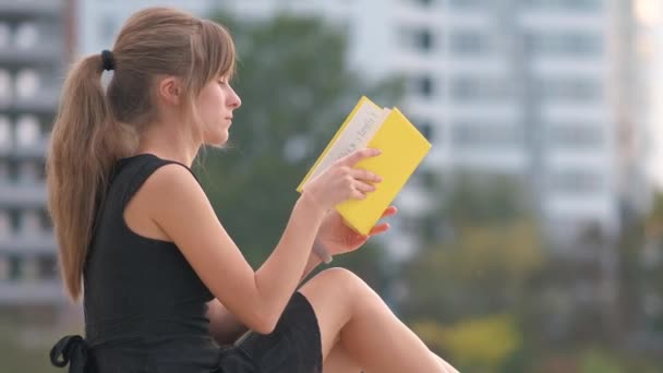Vrouwelijke studente die buiten in het zomerpark zit te lezen. Onderwijs- en opleidingsconcept. - Video