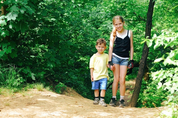 Une belle jeune fille et son frère se reposent en marchant dans les bois. Ils apprécient le beau temps d'été. Un garçon et une fille habillés en short en denim - Photo, image