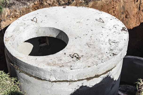 Instalación de pozos de alcantarillado de hormigón en el suelo en el sitio de construcción. El uso de anillos de hormigón armado para pozos negros, tanques sépticos de desbordamiento. Mejora de pozos y aguas residuales pluviales - Foto, imagen