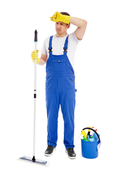 Konzept harter Arbeit - Ganztägiges Porträt eines müden Mannes, der in blauer Uniform den Boden reinigt, mit Mopp auf weißem Hintergrund isoliert - Foto, Bild