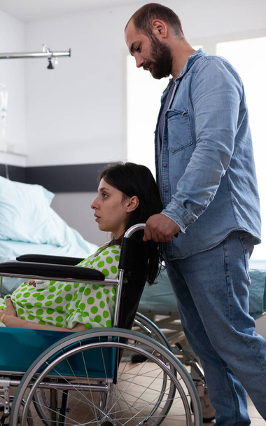 Kaukasischer Mann hilft schwangerer Frau im Rollstuhl - Foto, Bild