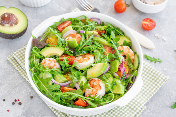 Delicious fresh salad with prawns, tomatoes, avocado, cucumber and onions in a bowl on a gray concrete background. Healthy dish. Top view, copy space - Photo, image
