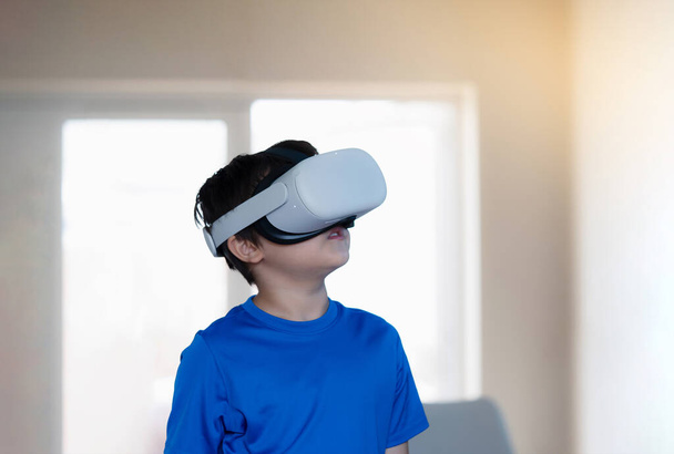 Amazed young kid wearing virtual reality goggles. Emotional Boy playing video games looking in VR headset. Portrait of Mixed race boy experiencing 3D gadget in living room. - Photo, Image