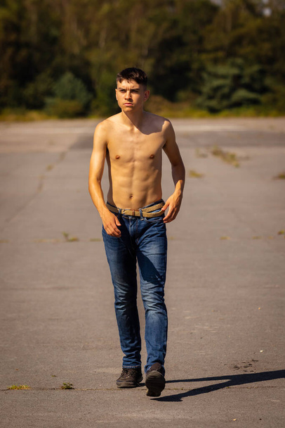 An eighteen year old teenage boy walking on a warm summer's day while in jeans and shirtless - Valokuva, kuva