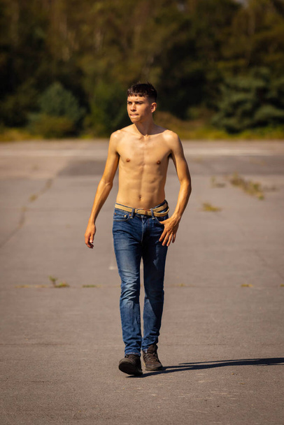 An eighteen year old teenage boy walking on a warm summer's day while in jeans and shirtless - 写真・画像