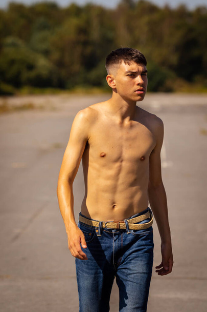 An eighteen year old teenage boy walking on a warm summer's day while in jeans and shirtless - Photo, Image
