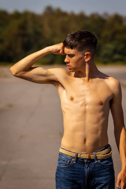 An eighteen year old teenage boy flexing his arm muscles on a warm summer's day while  shirtless - Photo, Image