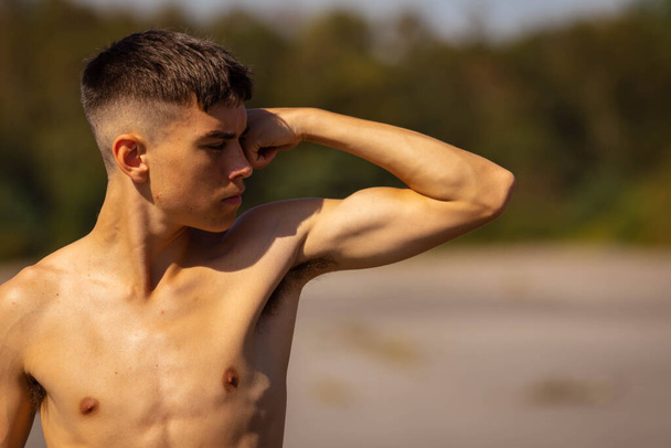 An eighteen year old teenage boy flexing his arm muscles on a warm summer's day while  shirtless - Фото, зображення