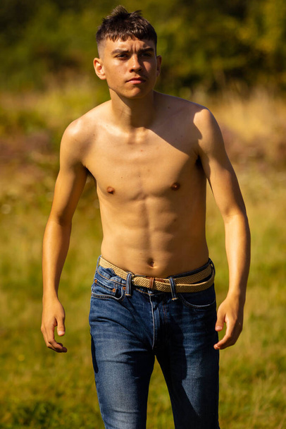 An eighteen year old teenage boy walking in a park on a warm summer's day while shirtless - Fotó, kép