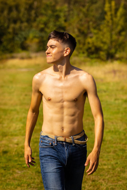 An eighteen year old teenage boy walking in a park on a warm summer's day while shirtless - Photo, image