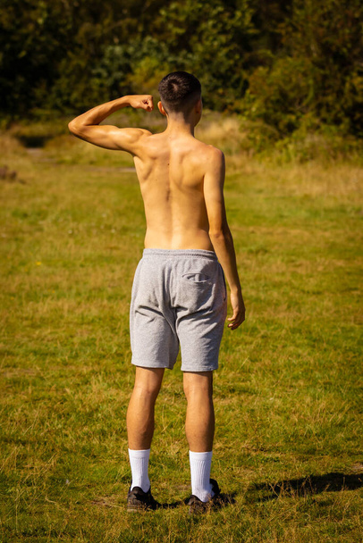 An eighteen year old teenage boy flexing his muscles on a warm summer's day wearing shorts and shirtless - Φωτογραφία, εικόνα