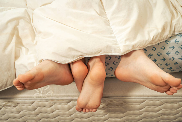 πόδια ενός ζευγαριού κάτω από την κουβέρτα. - Φωτογραφία, εικόνα