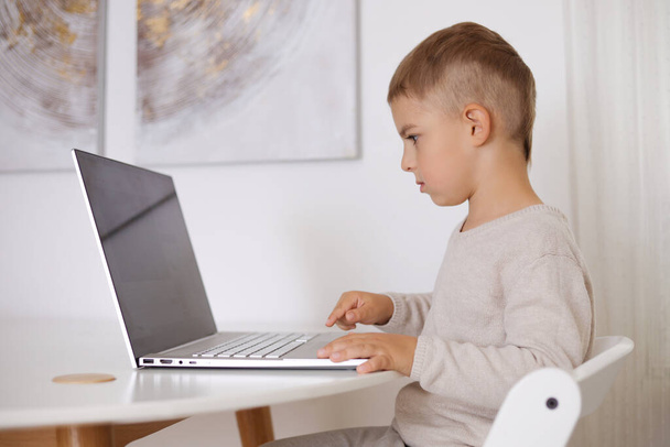 Onnellinen pieni poika pelaa peliä läppärillä kotona. Muotokuva lapsen kotona katsomassa sarjakuva tietokoneella. Nykyaikainen lasten ja koulutuksen teknologia. - Valokuva, kuva