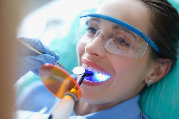Mulher em óculos de segurança em tratamento no dentista usando lâmpada de luz - Foto, Imagem