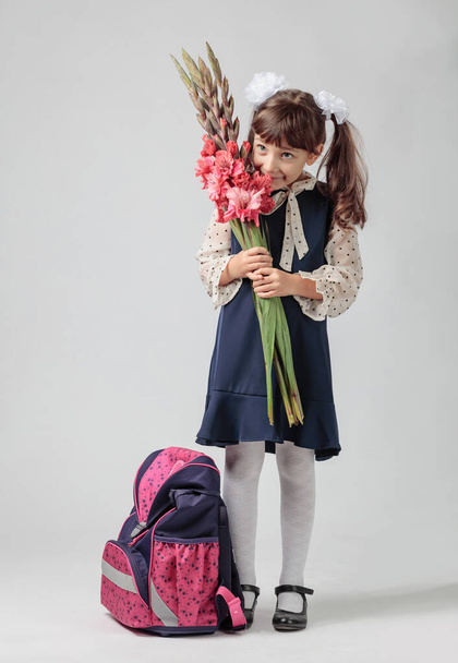 Retrato de una niña con uniforme de escuela primaria. Un estudiante de primer grado con una mochila y flores. Copiar espacio. - Foto, Imagen