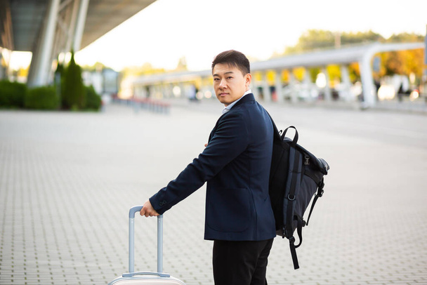 Successful asian businessman near airport and bus station goes with suitcases serious tourist looking at camera - Fotoğraf, Görsel