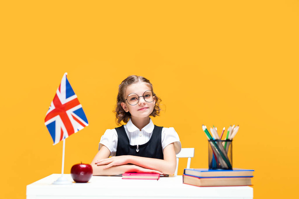 Smiling schoolgirl sitting at the desk with notebook during English lesson. Great Britain flag - Valokuva, kuva