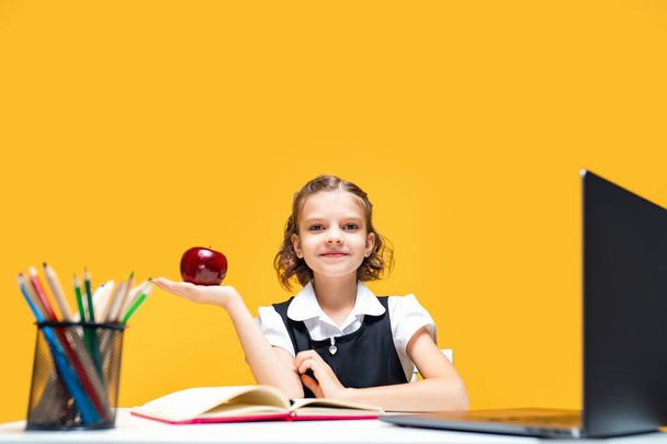 Little schoolgirl holding an apple in hand while change at online lesson. Distance education  - Zdjęcie, obraz