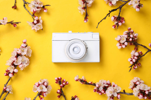 黄色の背景に美しい白い花の枝を持つカメラ。春のコンセプト。フラットレイアウト、トップビュー - 写真・画像