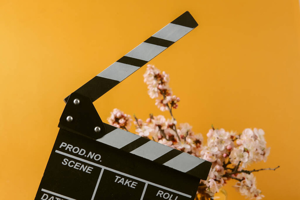 Film clapperboard und Schöne blühende Zweige auf orangefarbenem Hintergrund. - Foto, Bild