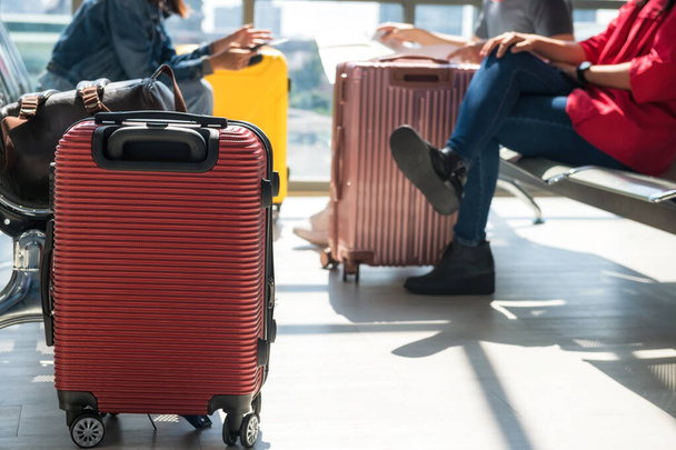la maleta roja de primer plano o el equipaje con pasajeros borrosos se sientan en el asiento de espera para esperar la salida en la terminal del aeropuerto. turista vacaciones o vacaciones en concepto. - Foto, Imagen