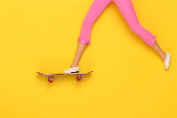 Les jambes de poupée roulent sur une planche à roulettes sur fond jaune. Minimalisme - Photo, image