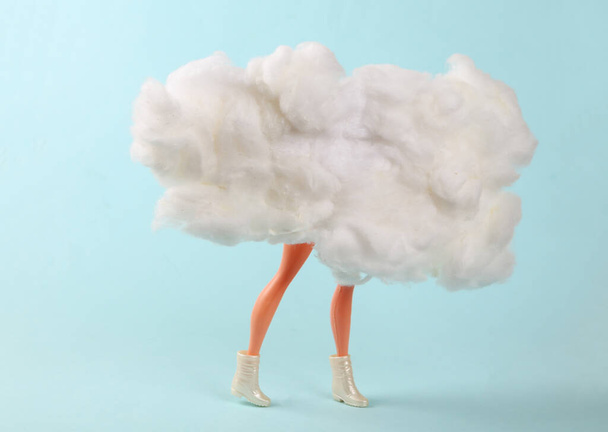 Doll legs behind the clouds on a blue background. Minimalism - Photo, Image