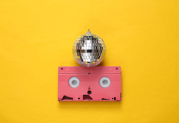 Disco bal met retro videocassette op gele achtergrond. Minimalistisch partijconcept - Foto, afbeelding