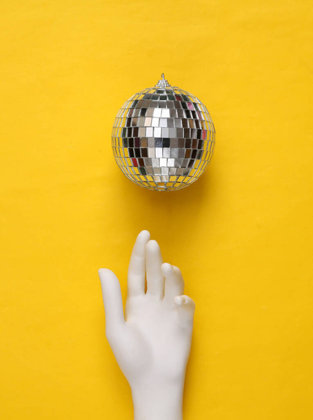 Bola de disco e mão sobre fundo amarelo. Conceito de partido minimalismo - Foto, Imagem