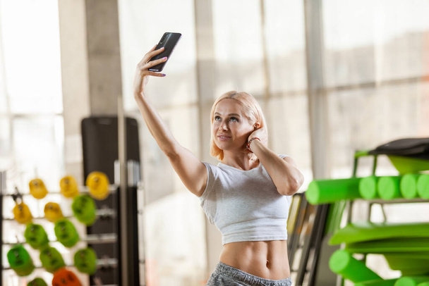Uśmiechnięta kobieta robi selfie na smartfonie w lekkiej siłowni - Zdjęcie, obraz