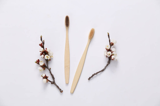 Eco bamboo toothbrushes and beautiful white flowering branches on white background. Springtime, eco concept. Flat lay, top view. - Фото, зображення