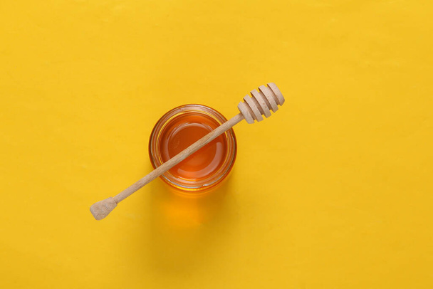 Pot de miel avec cuillère sur fond jaune. Vue de dessus. Pose plate - Photo, image