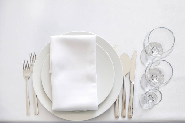 White table setting from above. Elegant empty plate, cutlery, napkin and glass. - Fotó, kép