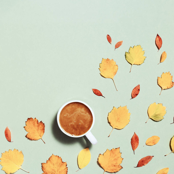Egy csésze kávé tejjel és piros sárga őszi levelek pasztell zöld papír háttér. Ősz, őszi kompozíció, lapos fektetés, felülnézet, másolás tér - Fotó, kép
