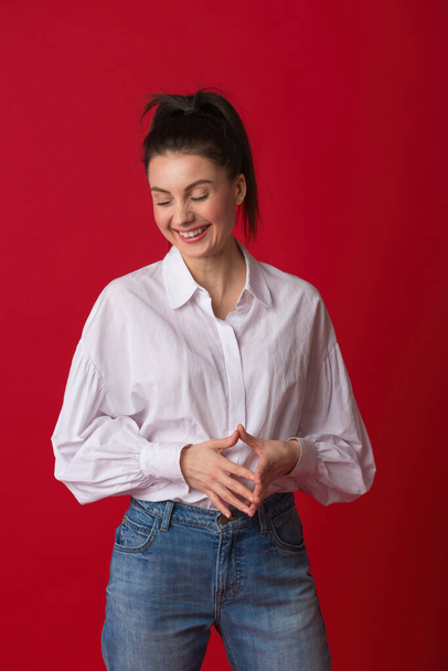 Happy young woman smiling. Female in 30s wearing casual white shirt and classic blue jeans in studio and looking away from camera. - Zdjęcie, obraz