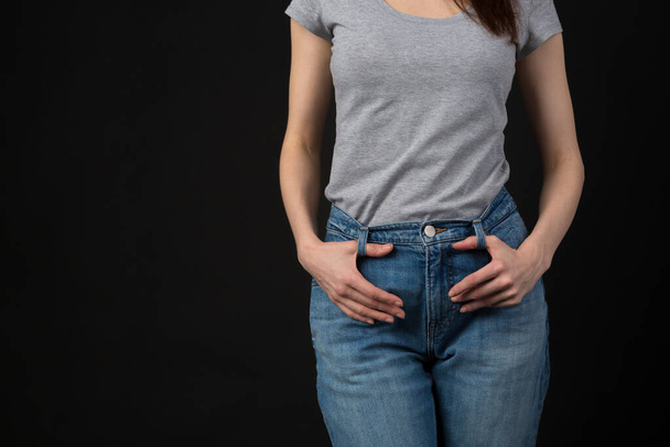 Slim young woman wearing classic blue jeans and casual grey shirt in studio. Unrecognizable female model body part with hands on her waist - Foto, Imagem