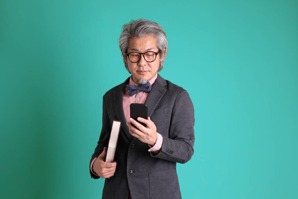 Starší asijský učitel stojící na zeleném pozadí. - Fotografie, Obrázek