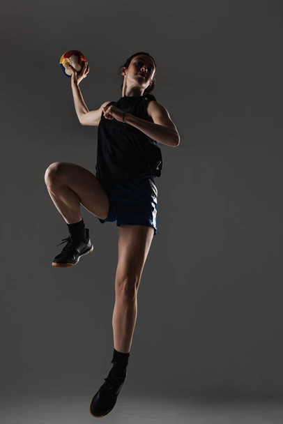 Handball player posing on gray background. Girl jumping with ball. - Foto, afbeelding