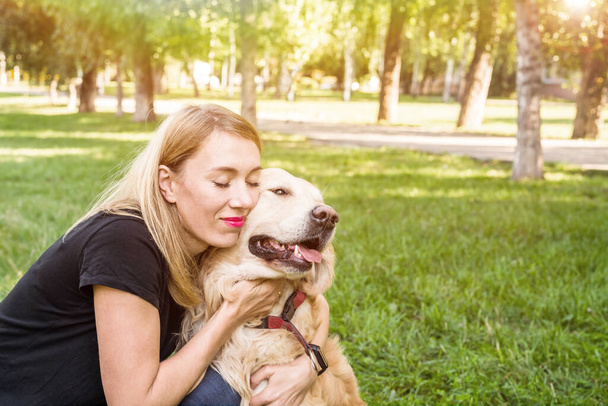 Young blond woman hugs her dog. Dog breed retriever with a girl in the park. - Фото, зображення