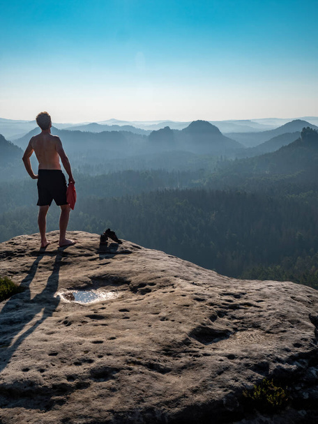 Безсоромний чоловік зі спортивною фігурою на краю скелі насолоджується видом на ранковий пейзаж
. - Фото, зображення