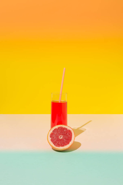 Yellow, red and blue summer background copy space with grapefruit slice and glass of grapefruit juice with a pink straw. Refreshment concept. - Photo, Image