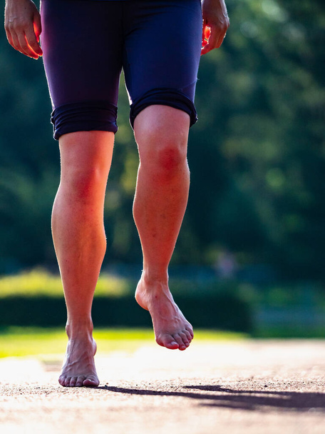Sólidos pies desnudos de una mujer de entrenamiento duro. Una mujer corre a lo largo de la superficie blanda de una pista de atletismo en leggins cortos. - Foto, imagen